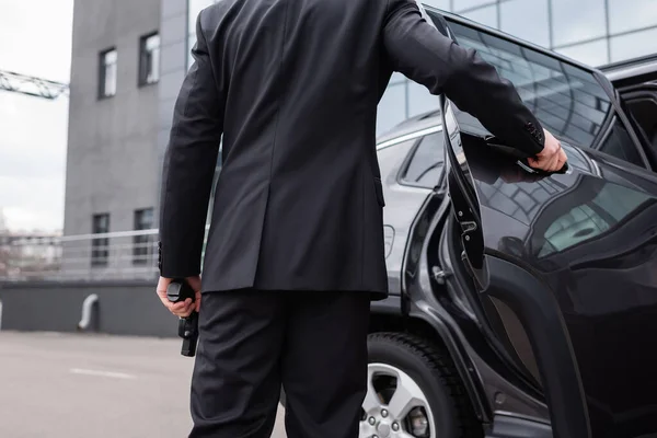 Back view of bodyguard in suit holding gun and opening car door — Stock Photo