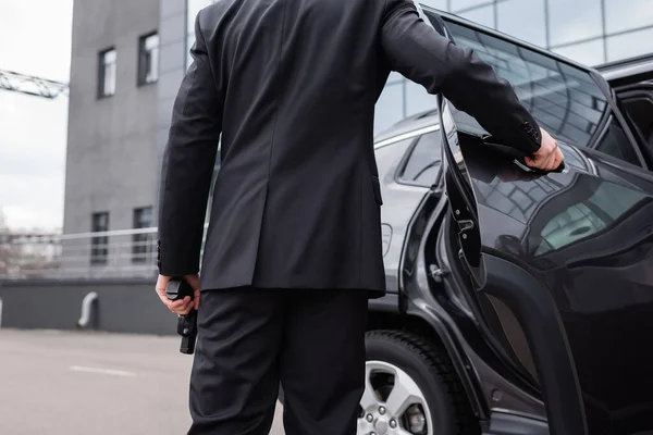 Vista trasera del guardaespaldas en traje sosteniendo pistola y abriendo la puerta del coche - foto de stock