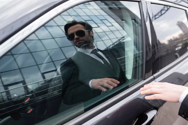 Reflexión de la salvaguardia barbuda en gafas de sol y puerta de apertura de traje en coche moderno - foto de stock