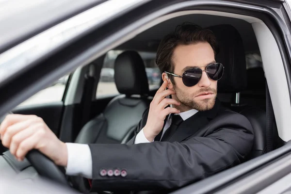 Salvaguardia barbuda en gafas de sol y traje de ajuste del auricular de seguridad en el coche - foto de stock