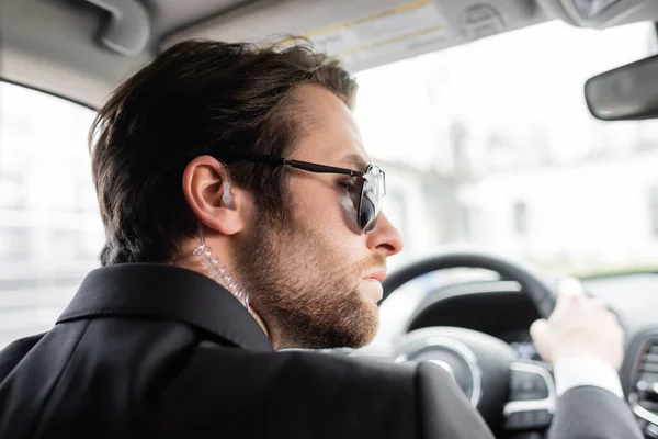 Bearded bodyguard in sunglasses driving modern automobile — Stock Photo