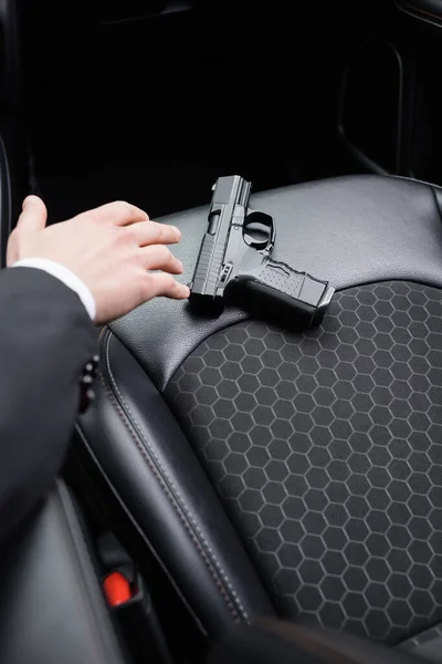 Cropped view of bodyguard reaching gun on seat of modern automobile — Stock Photo