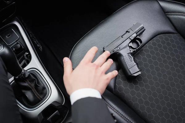 Top view of bodyguard reaching gun on seat of modern automobile — Stock Photo