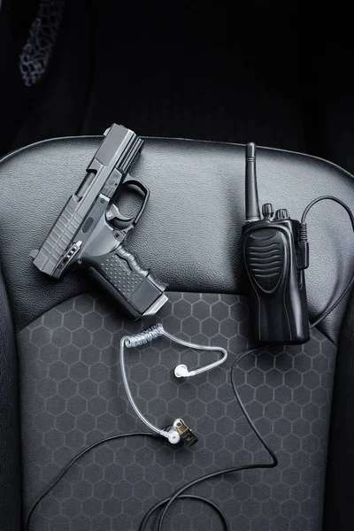 Top view of walkie talkie, gun and security earpiece on car seat — Stock Photo