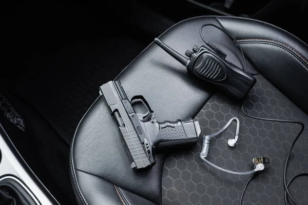 Top view of walkie talkie, black gun and security earpiece on car seat — Stock Photo