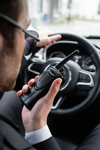 Garde du corps flou dans les lunettes de soleil en utilisant talkie walkie dans la voiture — Photo de stock