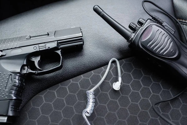 Close up of walkie talkie, black gun and security earpiece on car seat — Stock Photo