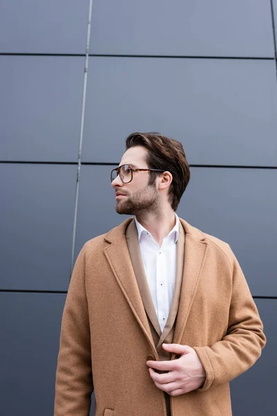 Hombre de negocios barbudo en gafas y abrigo beige de pie cerca del edificio exterior - foto de stock