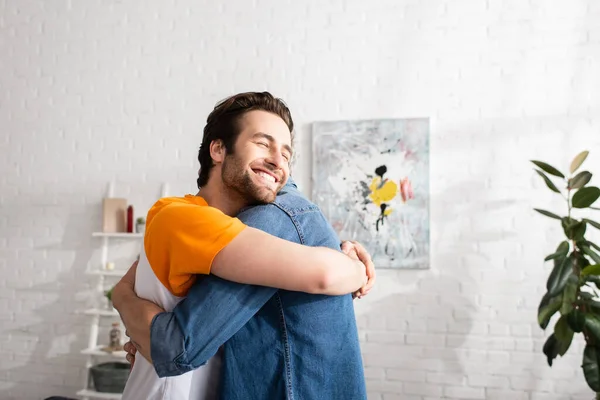 Jovem filho sorrindo e abraçando o pai em casa — Fotografia de Stock