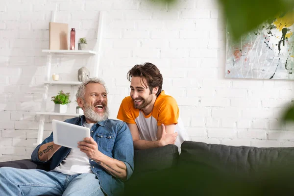 Cheerful father and son using digital tablet on couch at home — Stock Photo