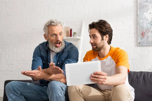 Hombre sosteniendo tableta digital cerca de padre asombrado - foto de stock