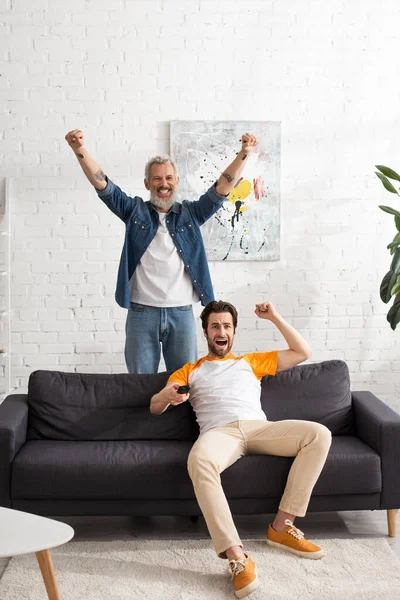 Emocionados padre e hijo viendo la televisión en casa - foto de stock