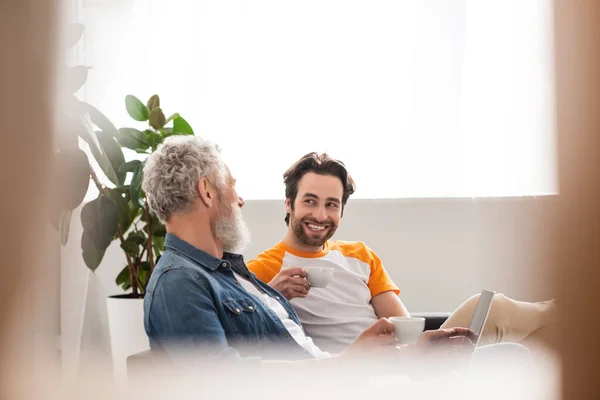 Reifer Mann spricht mit Sohn, der Kaffee in der Nähe von Laptop zu Hause hält — Stockfoto