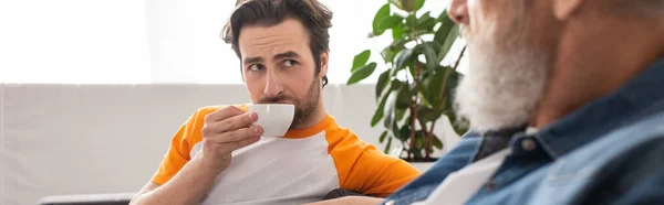 Homme avec tasse regardant le père flou à la maison, bannière — Photo de stock