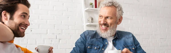 Homme mûr souriant au fils avec tasse de café à la maison, bannière — Photo de stock