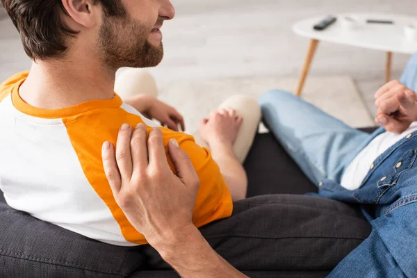 Vista recortada del hombre abrazando y señalando con el dedo cerca de sonreír hijo en el sofá - foto de stock