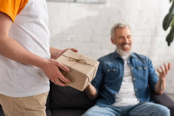 Hombre con presente de pie cerca de padre sobre fondo borroso - foto de stock