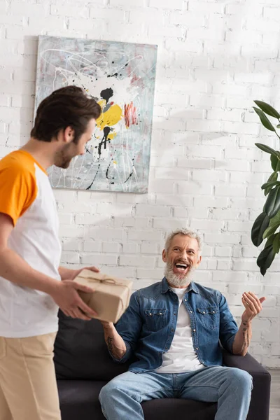 Cheerful mature man sitting near son with present on blurred foreground — Stock Photo