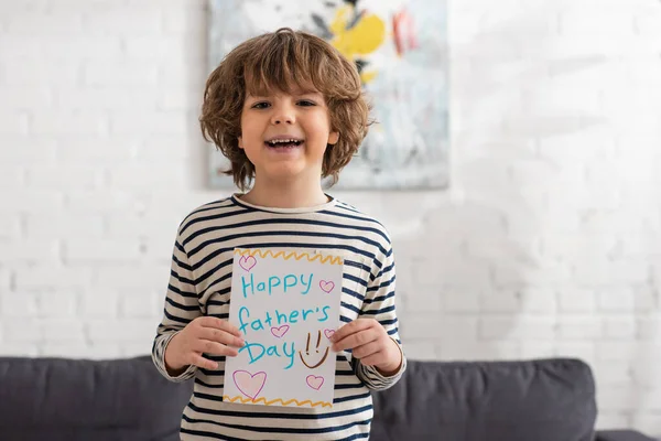 Sonriente niño sosteniendo tarjeta de regalo con feliz día de los padres letras - foto de stock