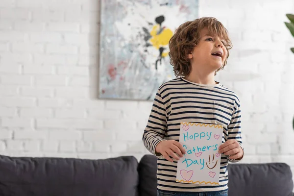 Chico alegre sosteniendo la tarjeta de regalo con letras del día de los padres felices - foto de stock