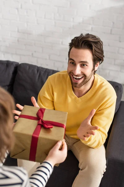 Son giving present to cheerful father on couch — Stock Photo