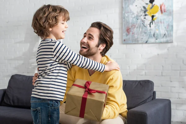 Cheerful kid hugging father with present on blurred foreground — Stock Photo