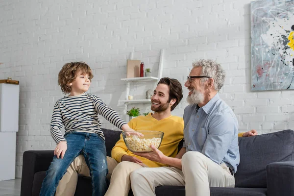 Men with popcorn sitting on couch near kid — Stock Photo