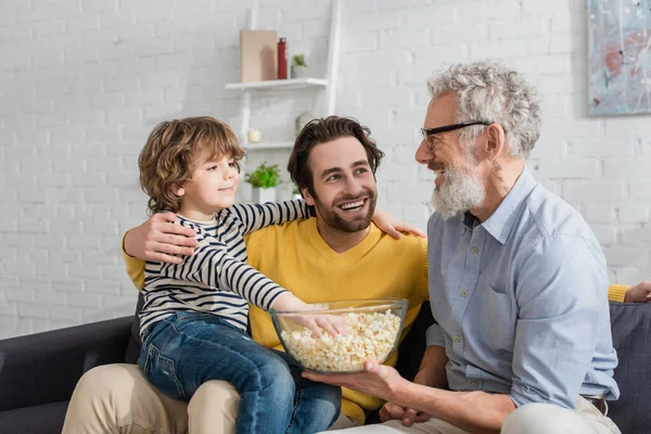 Mature man holding popcorn near grandson and son — Stock Photo