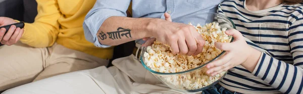 Vista ritagliata del ragazzo che tiene i popcorn vicino ai genitori con telecomando, banner — Foto stock
