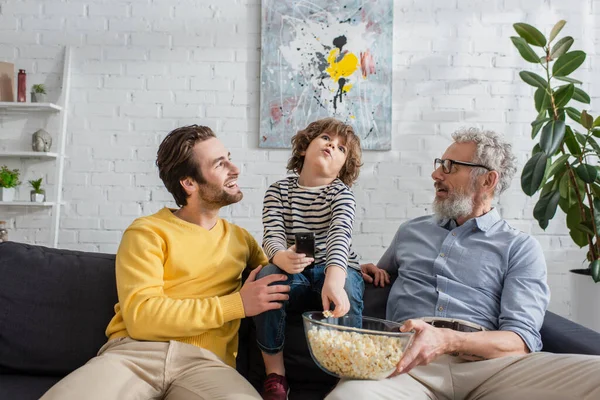 Eltern mit Popcorn schauen Kind mit Fernbedienung im Wohnzimmer an — Stockfoto