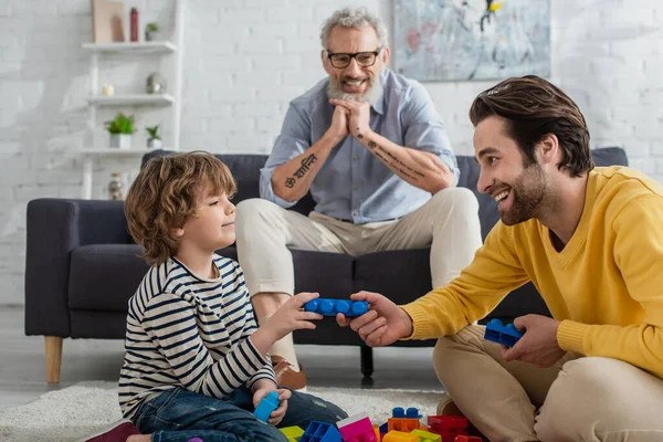 Smiling father and son playing building blocks near grandfather on couch — Stock Photo