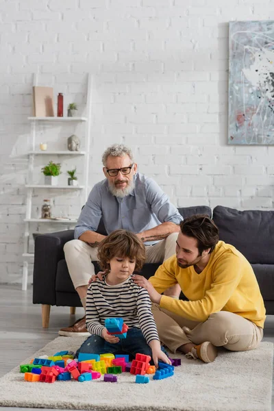 Uomo abbraccio figlio con blocchi di costruzione vicino nonno sul divano — Foto stock