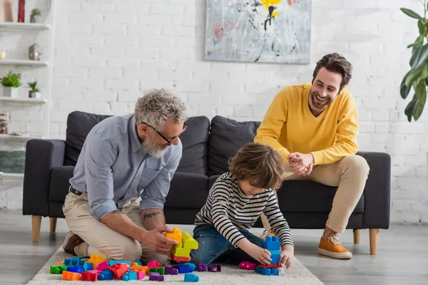 Lächelnder Opa spielt Bauklötze neben Kind und Sohn zu Hause — Stockfoto