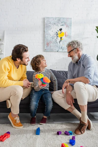 Smiling boy with building blocks looking at grandfather on couch — Stock Photo