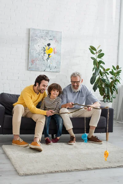 Smiling men and kid playing fishing in living room — Stock Photo