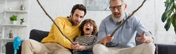Men and excited child playing toy fishing in living room, banner — Stock Photo