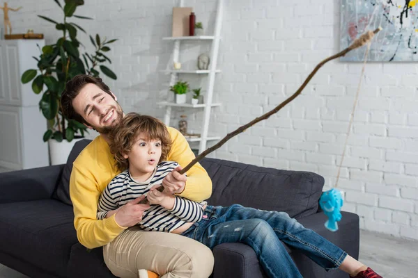 Eccitato bambino che gioca a pesca con la canna giocattolo vicino al padre — Foto stock