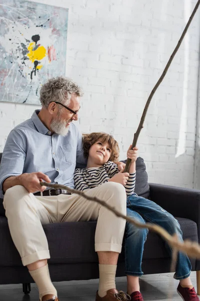 Sorridente nonno e ragazzo che tiene ramoscelli di legno a casa — Foto stock