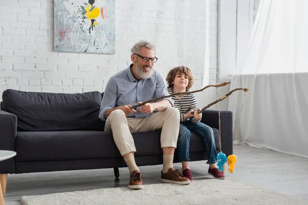 Grand-père positif avec canne à pêche jouet jouant avec petit-fils — Photo de stock