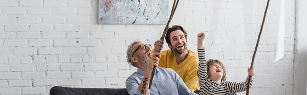 Excited men and boy holding wooden twigs at home, banner — Stock Photo