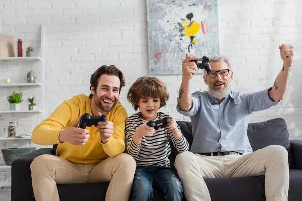 KYIV, UKRAINE - APRIL 12, 2021: Mature man showing yes gesture near son and grandson with joysticks — Stock Photo