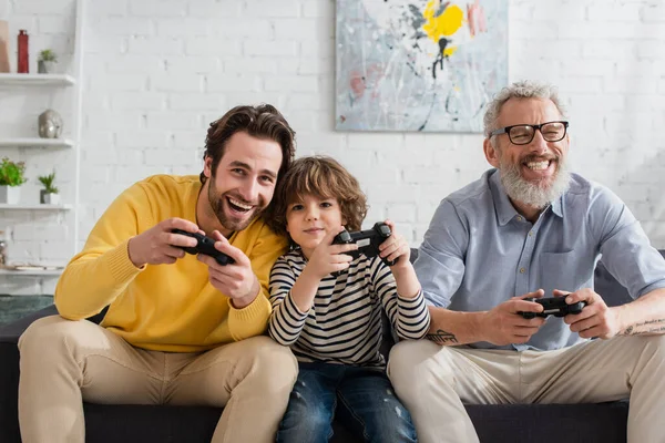 KYIV, UKRAINE - APRIL 12, 2021: Men and kid with joysticks playing video game at home — Stock Photo