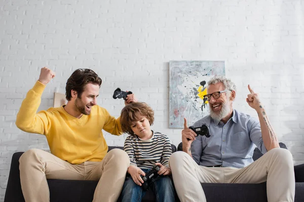 KYIV, UKRAINE - APRIL 12, 2021: Positive parents with joysticks sitting near upset boy — Stock Photo