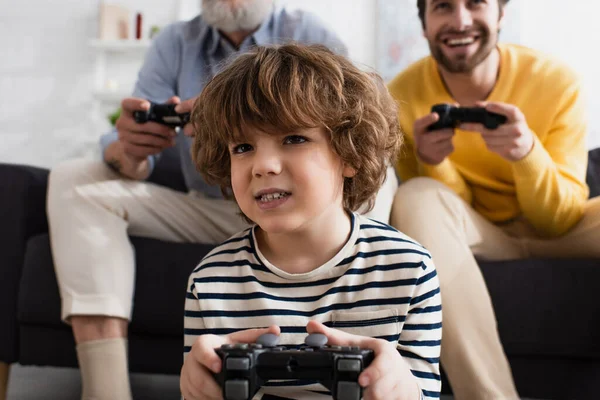 KYIV, UKRAINE - 12 AVRIL 2021 : Enfant concentré jouant à un jeu vidéo avec ses parents — Photo de stock