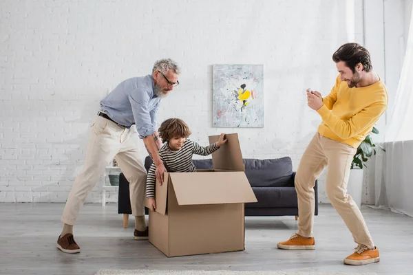 Smiling man taking photo of father and son playing with box — Stock Photo