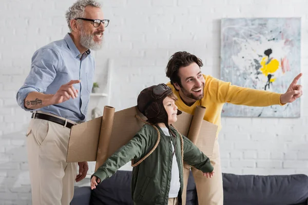 Lächelnder Vater zeigt mit Finger auf Kind im Fliegerkostüm und Opa — Stockfoto