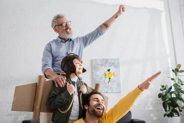 Aufgeregter Junge im Fliegerkostüm neben Papa und Opa — Stockfoto