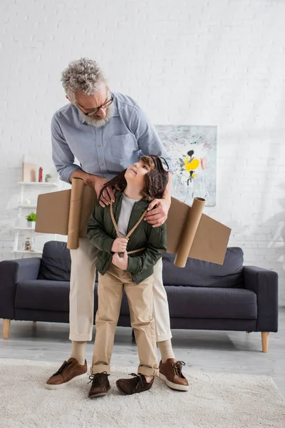 Reifer Mann blickt lächelnden Enkel im Fliegerkostüm an — Stockfoto