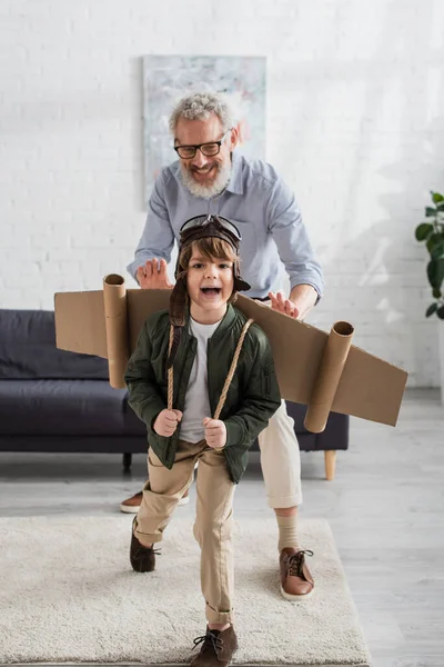 Happy boy in aviator helmet and wings playing with grandfather — Stock Photo