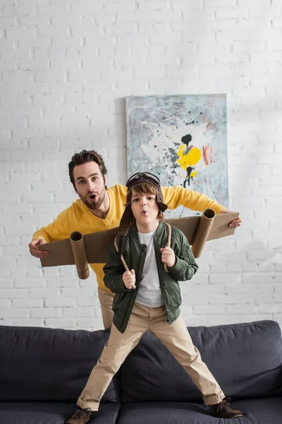 Père et enfant excités dans le casque et les ailes de l'aviateur regardant la caméra — Photo de stock